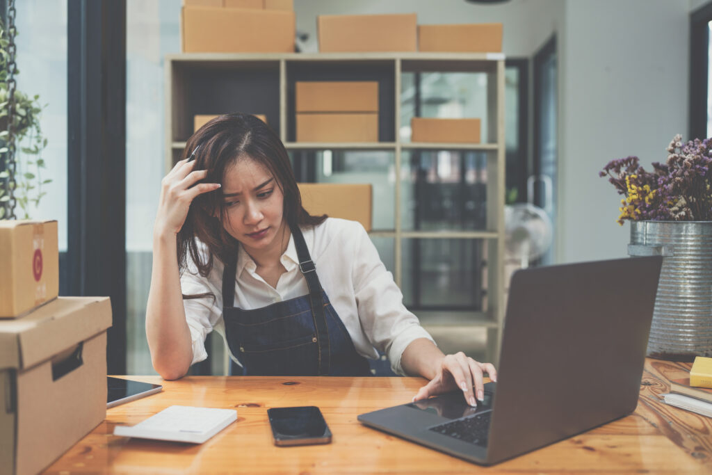 A woman looking down at a notepad with her hand on a laptop. She is visibly stressed.