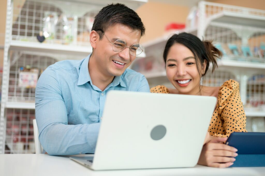 Two people looking at a computer together. The man on the left has a computer in front of him and the woman has a tablet in front of her. They are both looking at the computer.