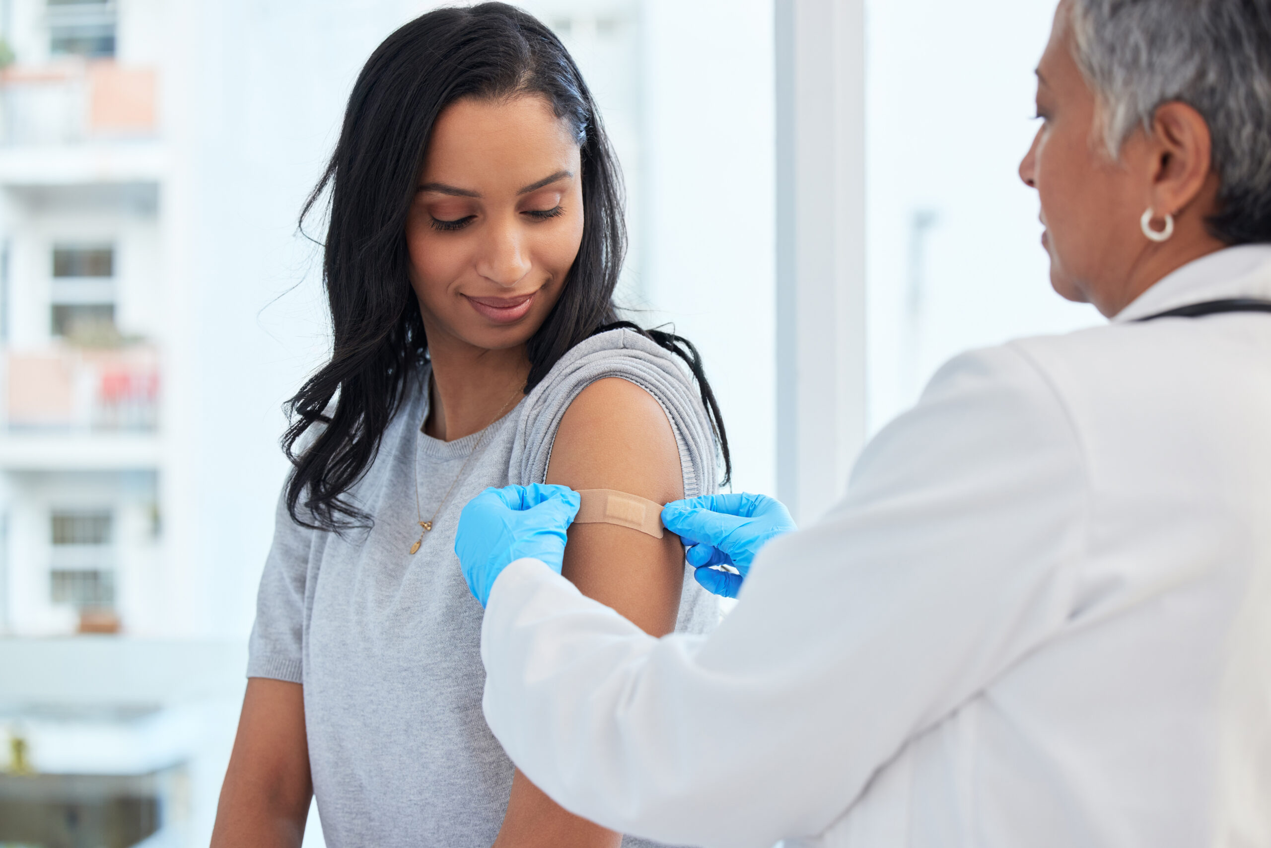 Doctor putting band aid on patient after administering vaccine.